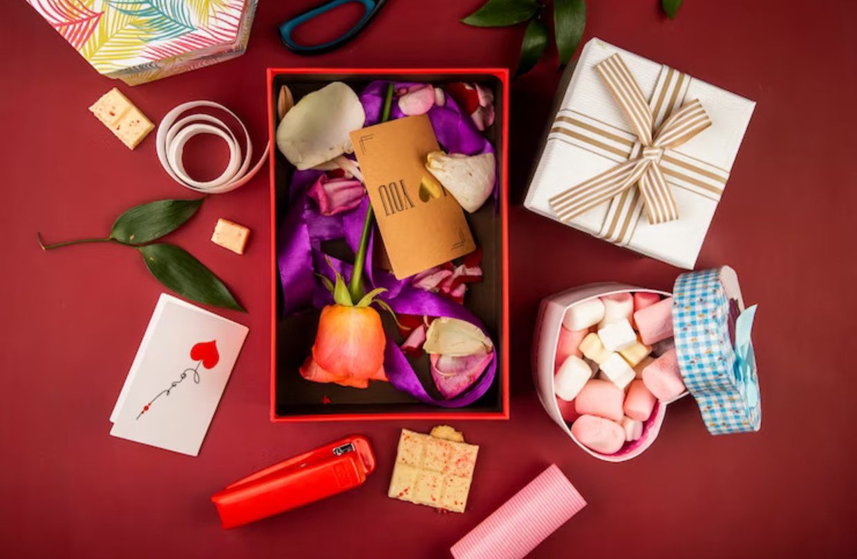 top-view-red-present-box-with-brown-paper-card-coral-color-rose-flower-petals-with-purple-ribbon-heart-shaped-box-filled-with-marshmallow-dark-red-table_141793-8803